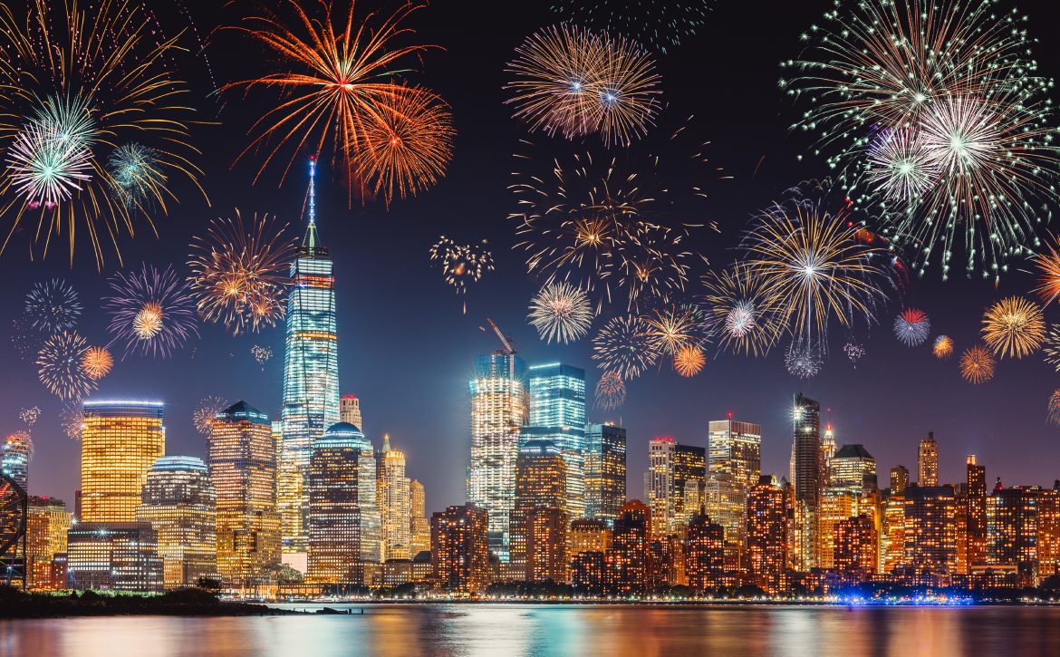 New Years Eve with colorful Fireworks over New York City skyline long exposure with dark blue-purple sky, orange city light glow and reflections in the river