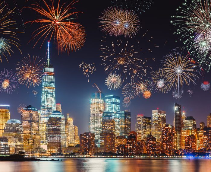 New Years Eve with colorful Fireworks over New York City skyline long exposure with dark blue-purple sky, orange city light glow and reflections in the river