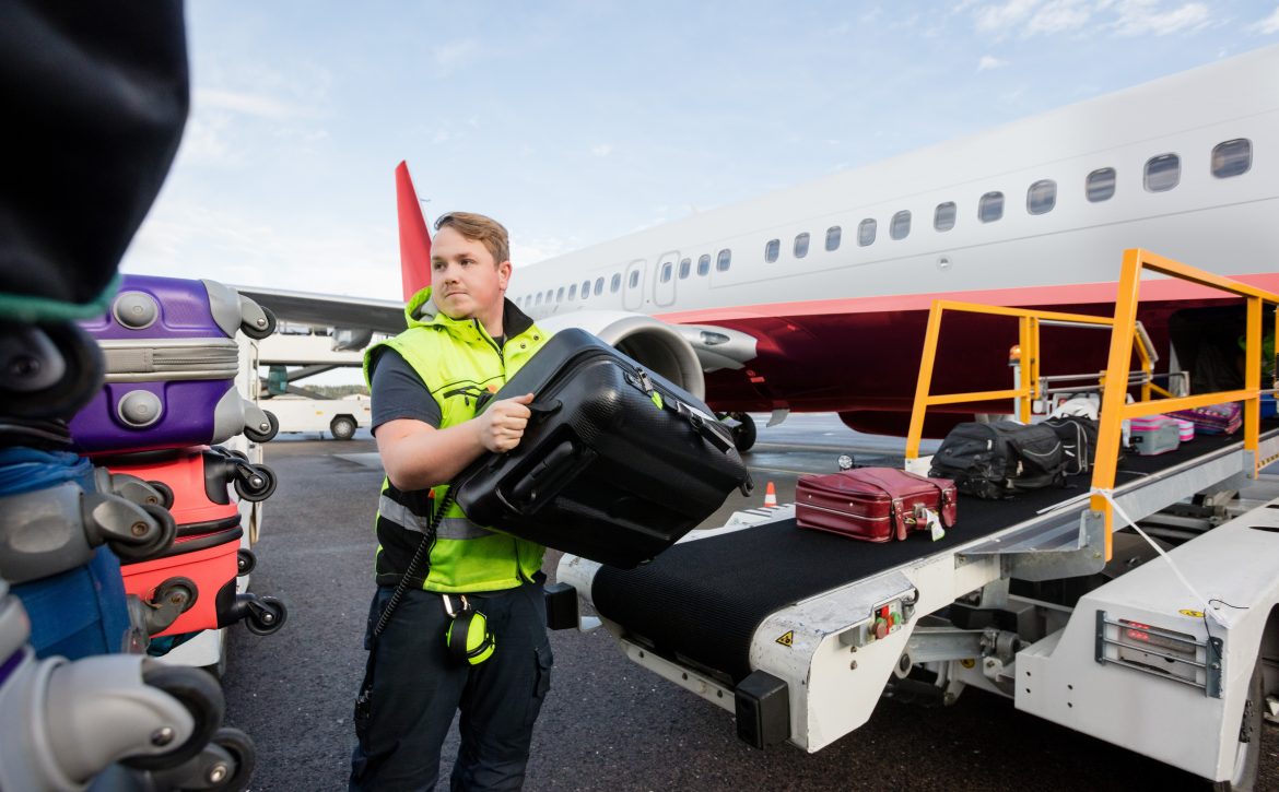 Worker Stacking Bags On Trailer At Runway