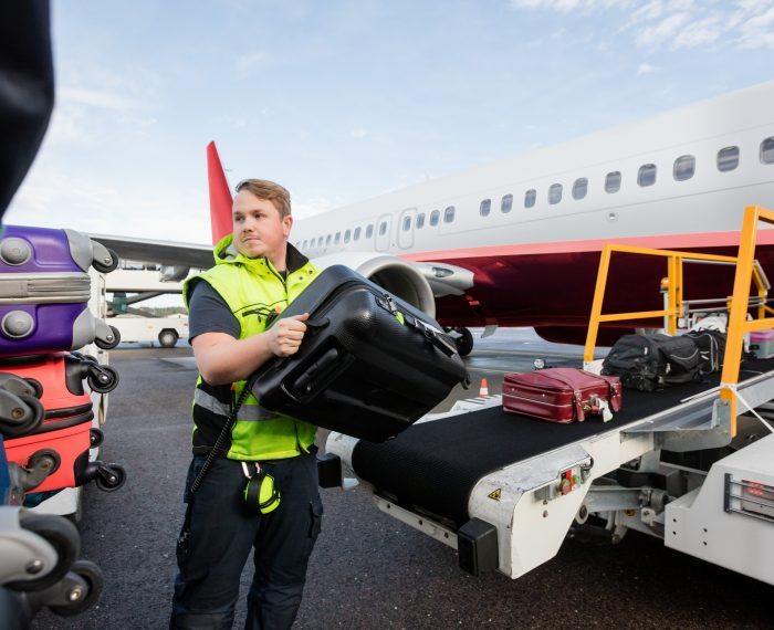 Worker Stacking Bags On Trailer At Runway