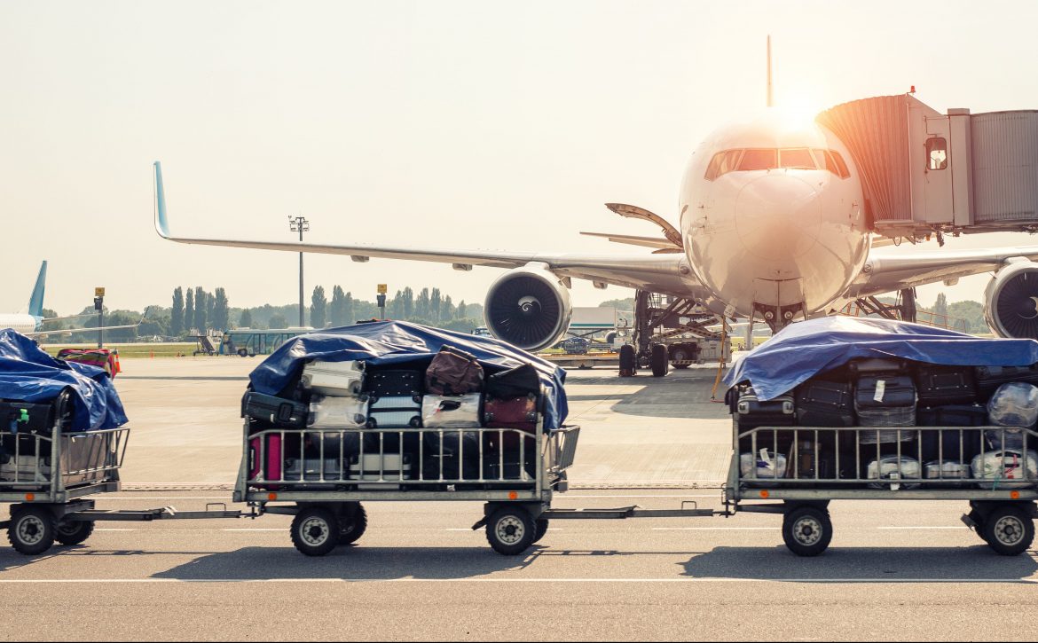 Luggage motion blurred trolley cart going fast delivering passenger baggage to modern plane on taxiway at airport on bright sunny day. Commercial aircraft on background at sunset or sunrise time