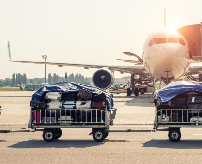 Luggage motion blurred trolley cart going fast delivering passenger baggage to modern plane on taxiway at airport on bright sunny day. Commercial aircraft on background at sunset or sunrise time