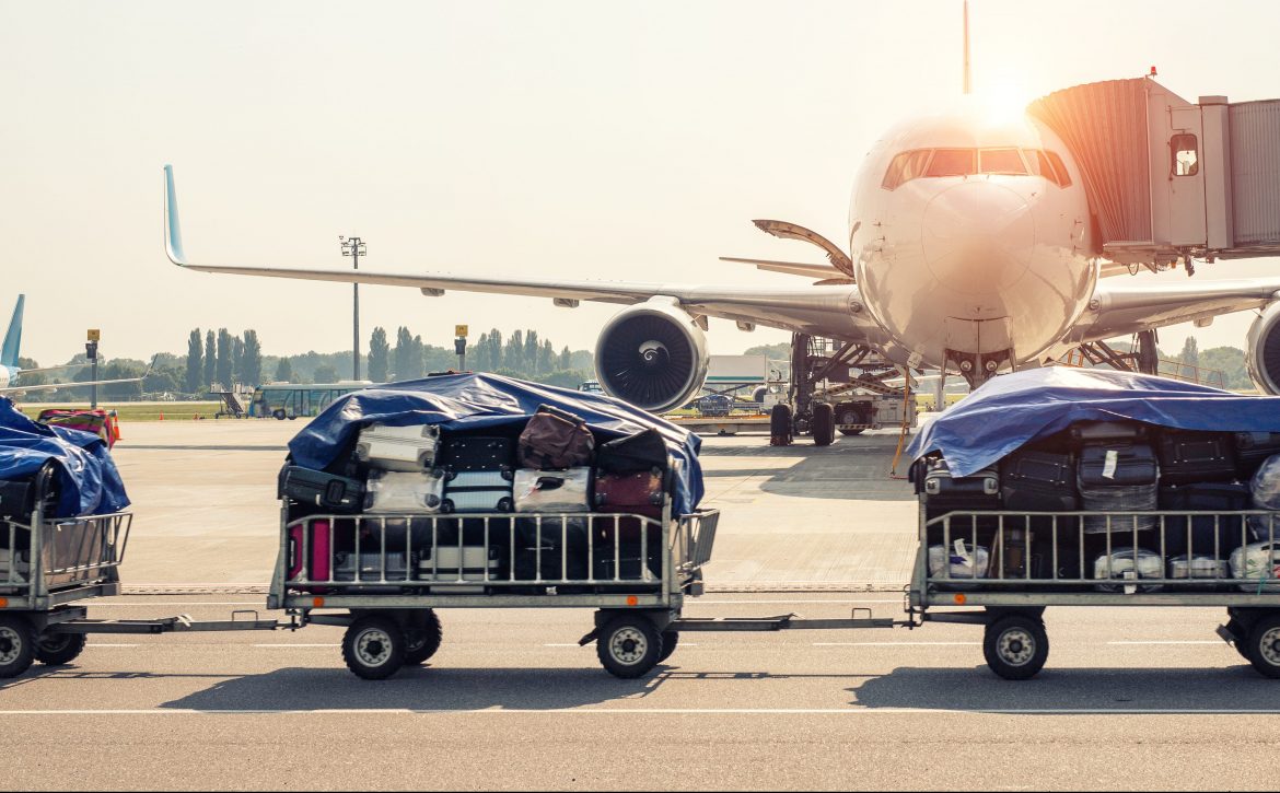 Luggage motion blurred trolley cart going fast delivering passenger baggage to modern plane on taxiway at airport on bright sunny day. Commercial aircraft on background at sunset or sunrise time