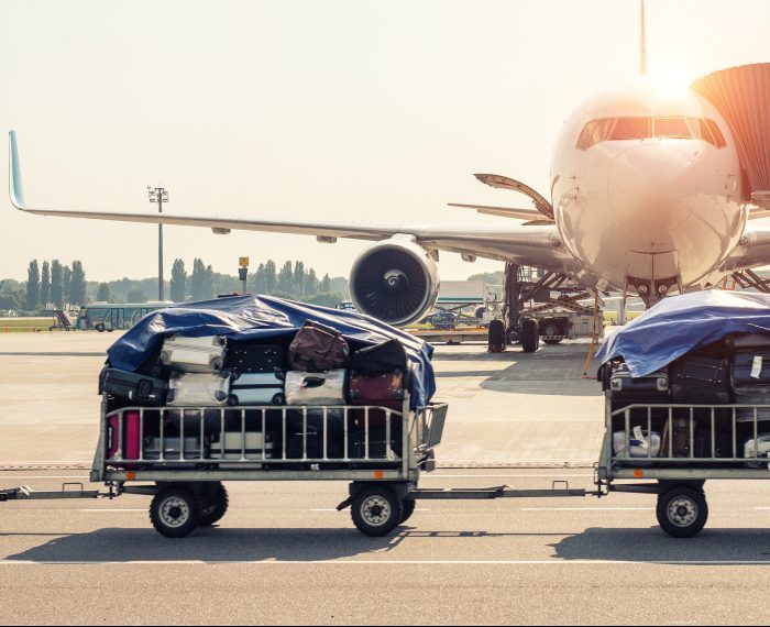 Luggage motion blurred trolley cart going fast delivering passenger baggage to modern plane on taxiway at airport on bright sunny day. Commercial aircraft on background at sunset or sunrise time